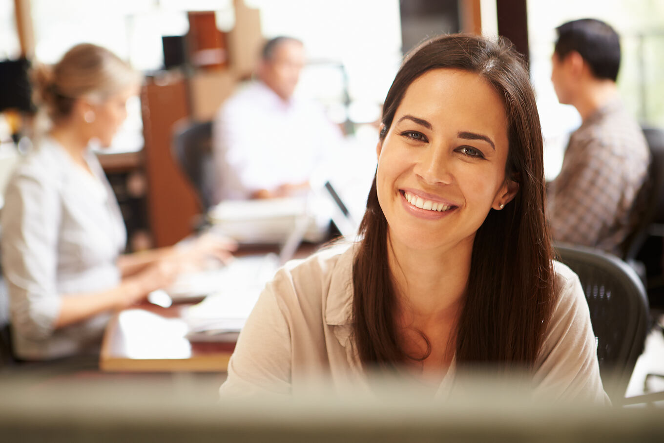 Businesswoman,Working,At,Desk,With,Meeting,In,Background